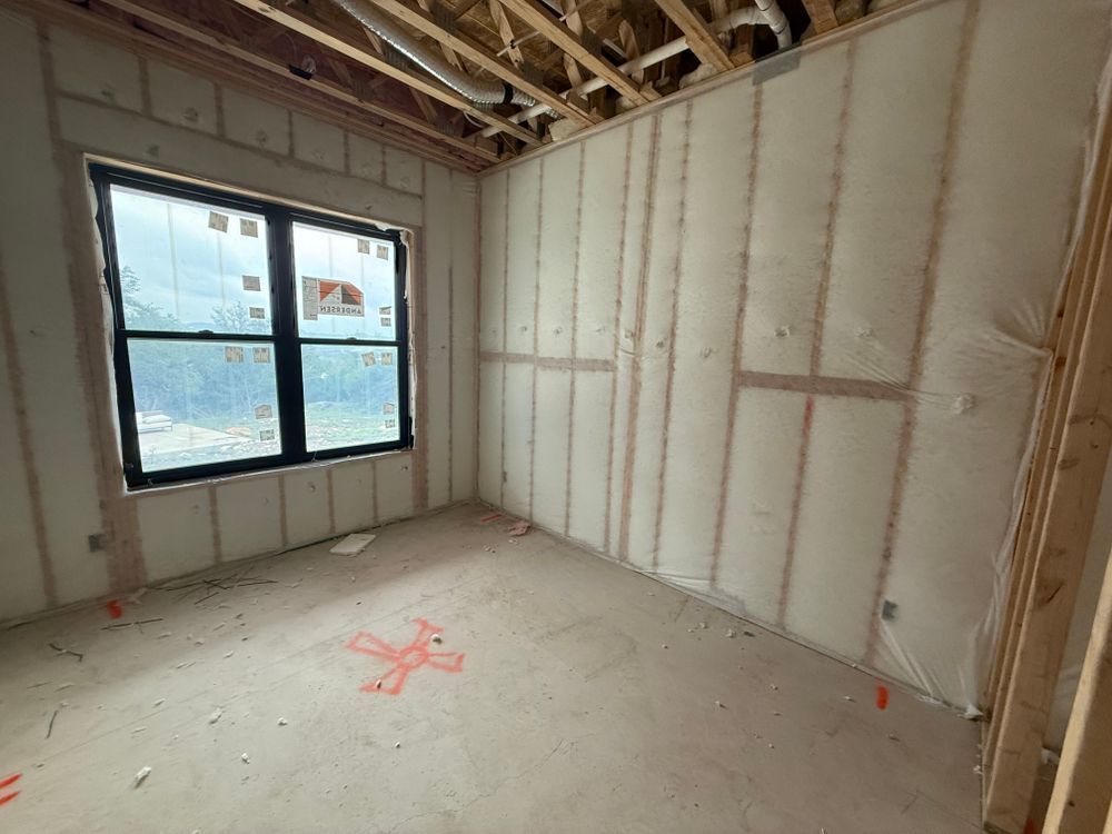Empty unfinished room with exposed insulation, bare framing, and a window.