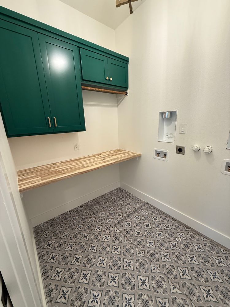 Empty laundry room with green cabinets, patterned tile floor, and a wood countertop.