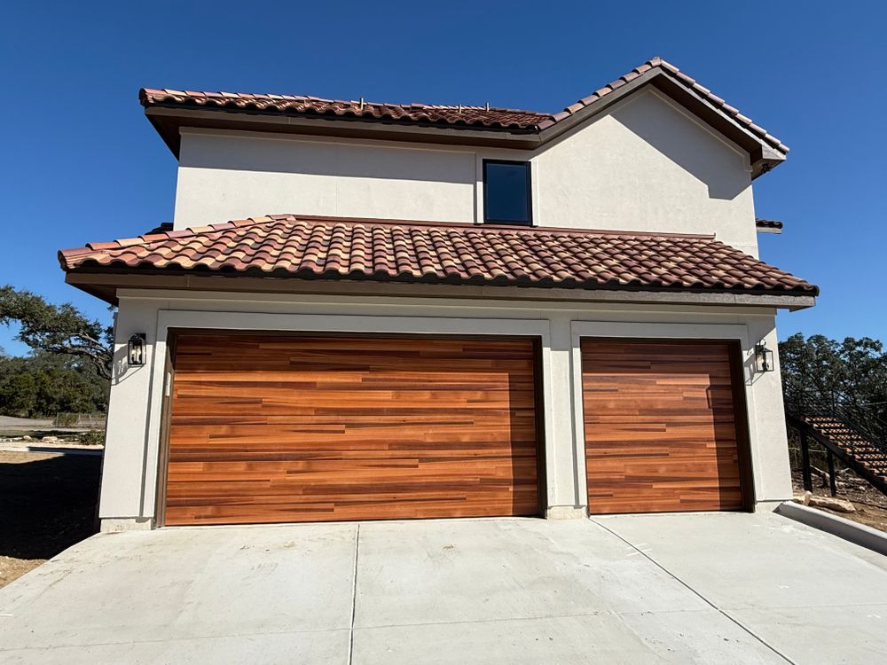 Two-story stucco house with terracotta roof and wooden garage doors under a blue sky