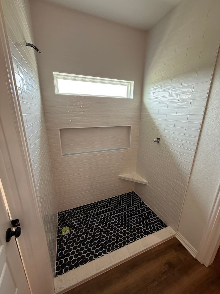 Small tiled shower stall with two narrow windows, white walls, and a black mosaic floor.