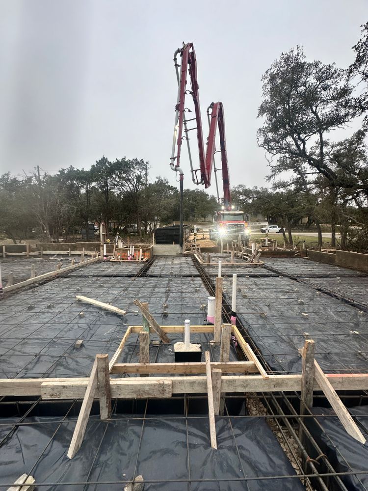 Concrete slab construction site with rebar, wooden forms, and a red pump truck in the background