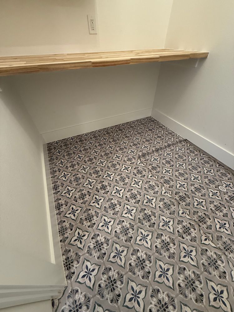 Small empty room with patterned tile floor, white walls, and a wooden shelf along the back wall