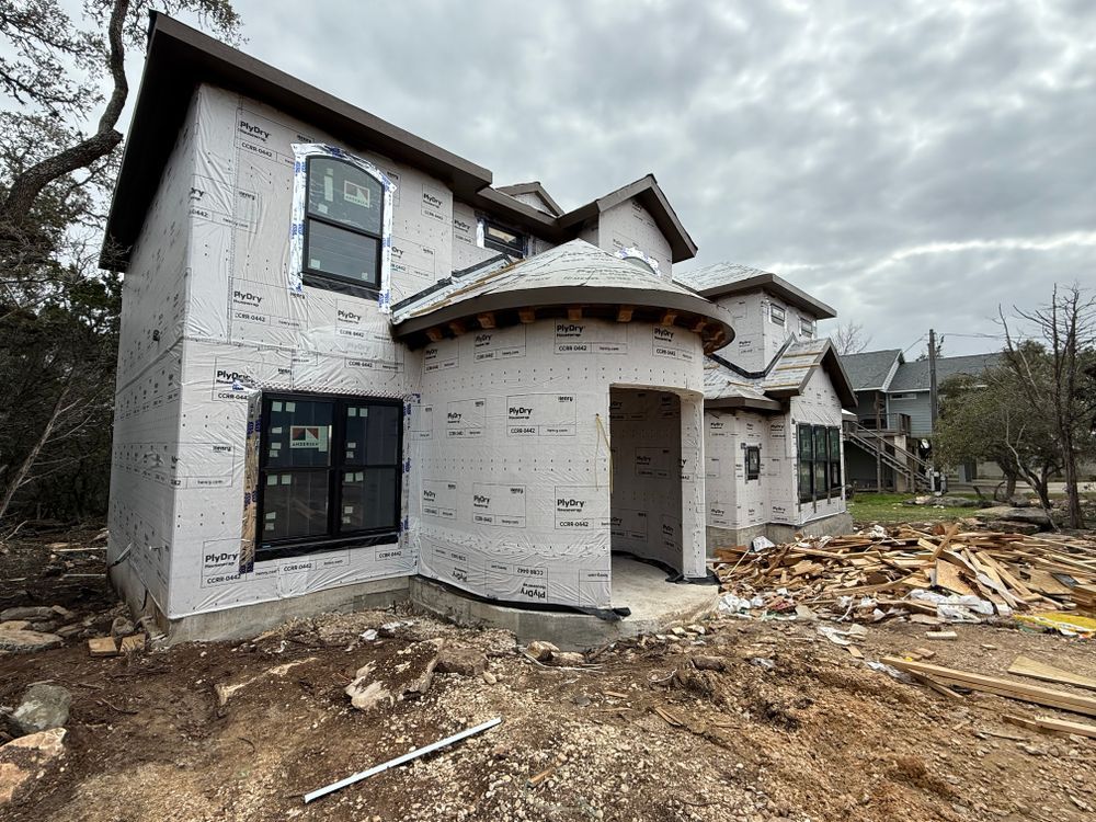 Unfinished two-story house under construction with exposed white exterior and debris in the front yard