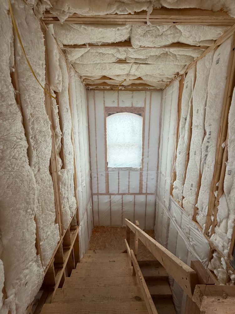 Insulated attic stairwell with exposed framing, narrow wooden stairs, and a frosted window at the end.