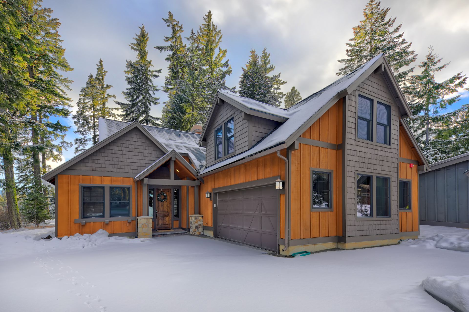 Snow-covered wooden cabin with gray roof and tall pine trees in the background