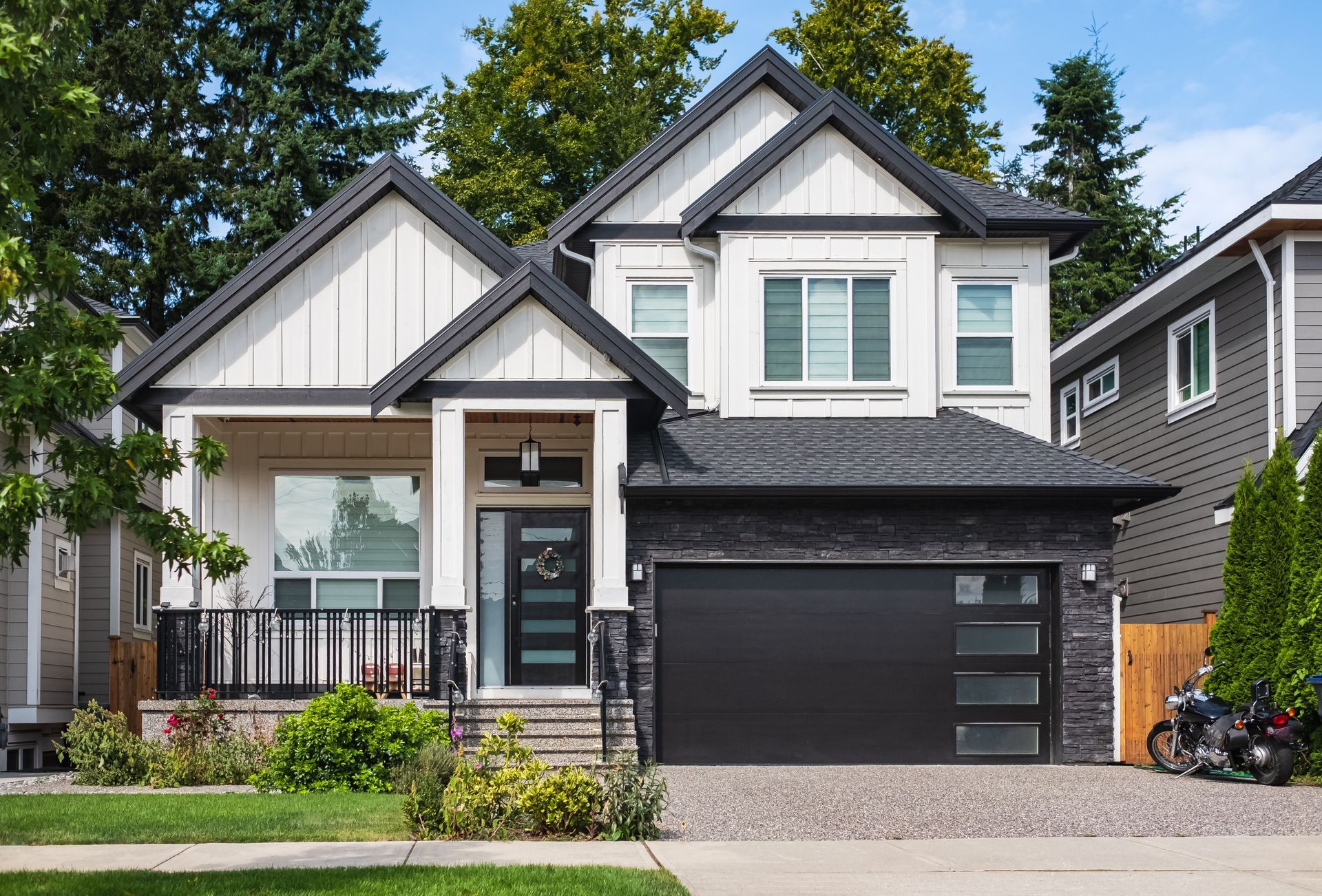 Modern two-story house with gray and white siding, black garage door, and front garden