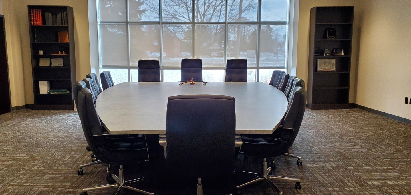 A conference room with a long table and chairs in front of a window.