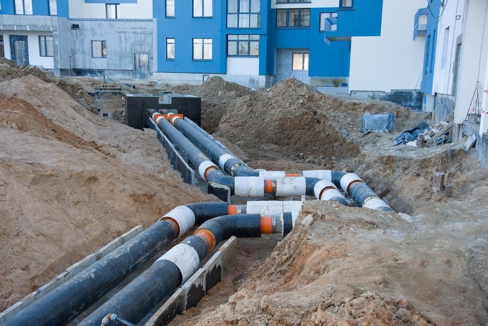 A Bunch of Pipes Are Laying in the Dirt in Front of a Building — Affordable Plumbing In Port Macquarie, NSW