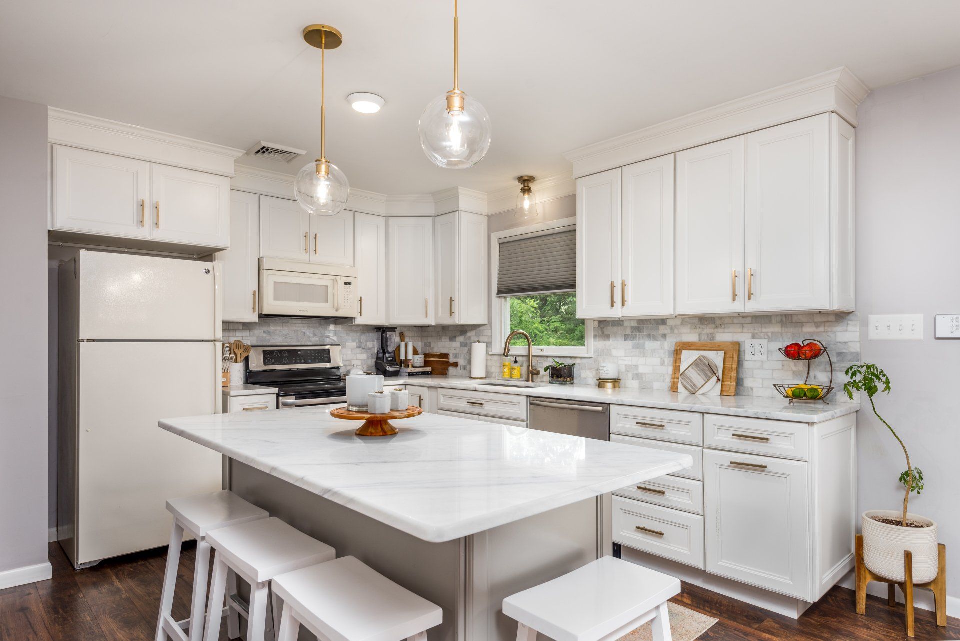 A kitchen with white cabinets , stools , a refrigerator , and a large island.
