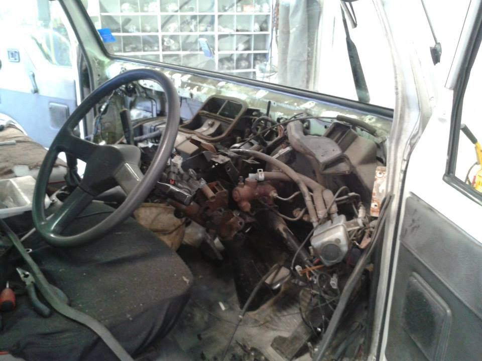 Interior of a light-coloured vehicle with dashboard components removed, revealing wires and mechanical parts; steering wheel visible. — Mechanic in Greenbank, QLD