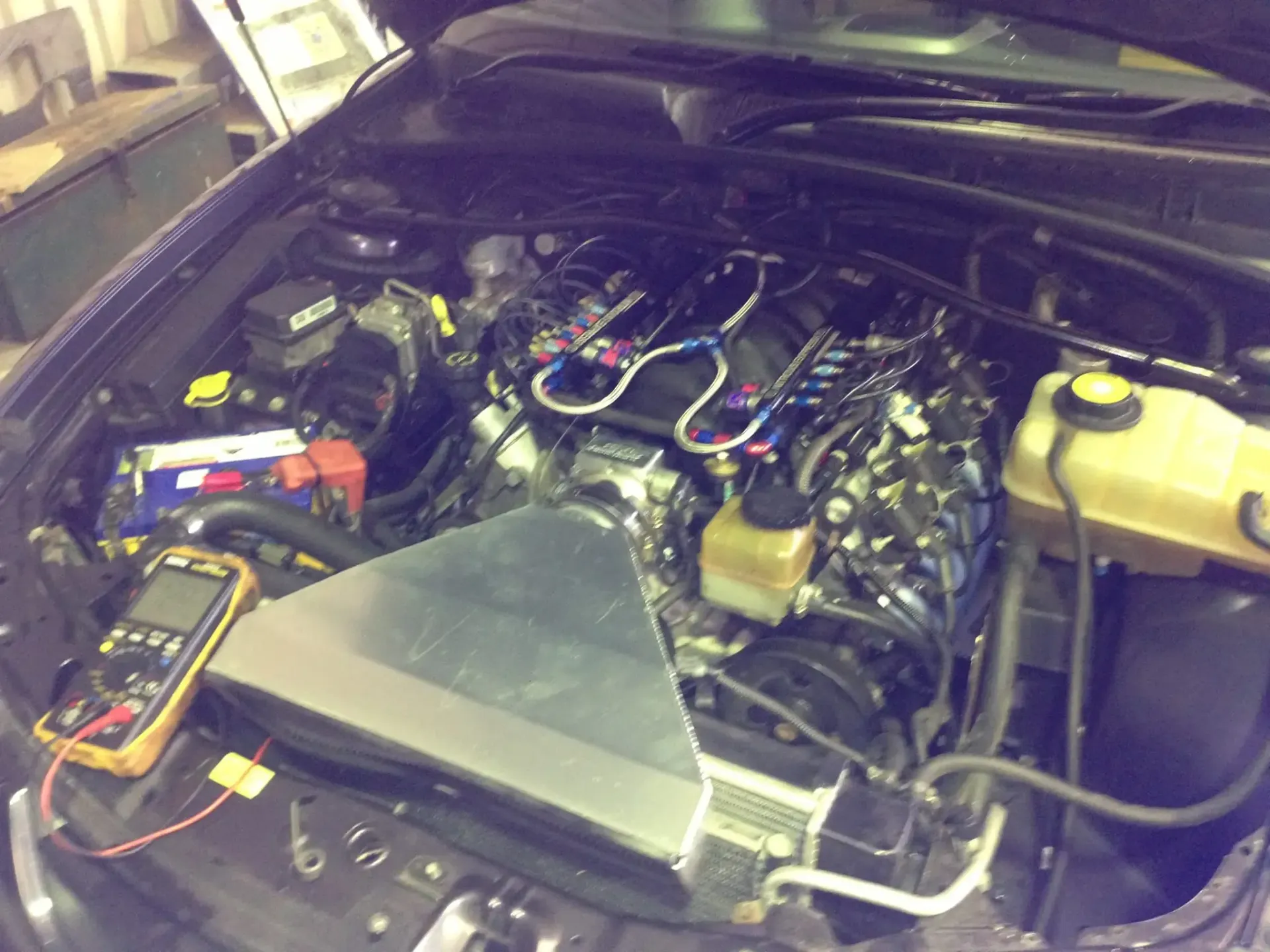 Car engine bay with an engine undergoing diagnostics, multimeter visible. — Mechanic in Port Macquarie, NSW