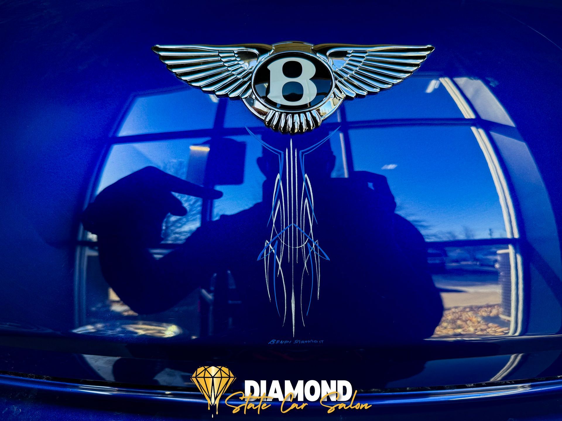Blue Bentley car hood with logo, person's reflection, and logo for Diamond Shine Auto Detail.