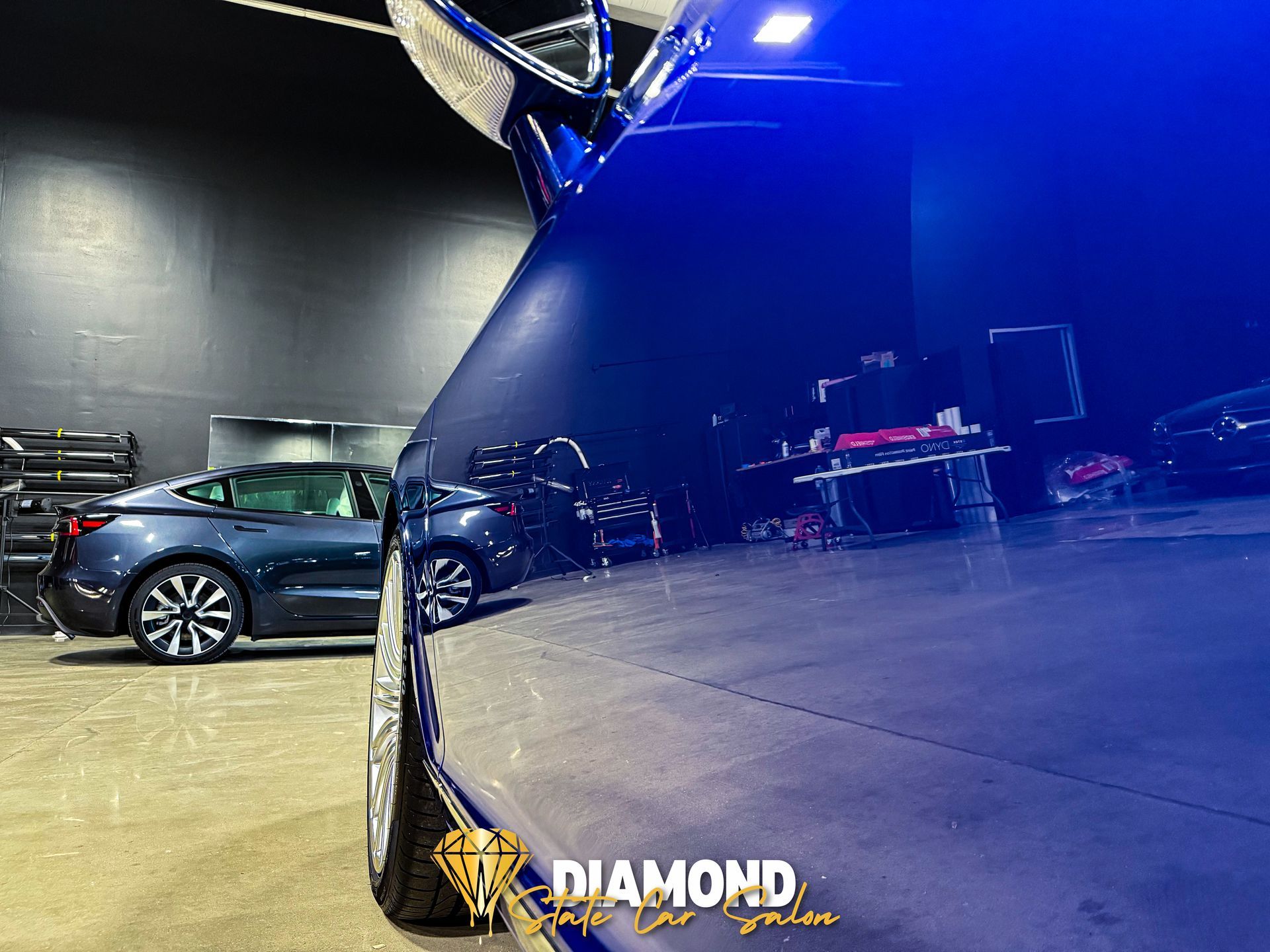 Blue car reflecting interior with Tesla in the background. Diamond logo visible.