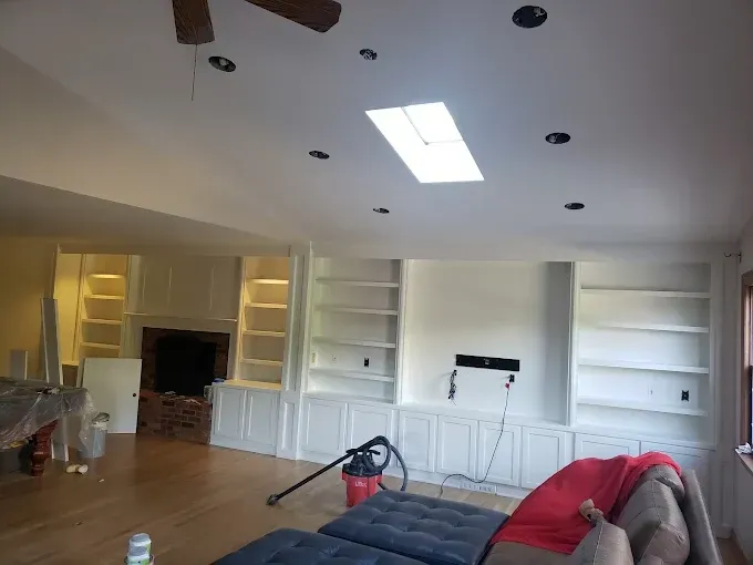 Living room with white built-in bookshelves, fireplace, and skylight. Vacuum cleaner and furniture are in the room.