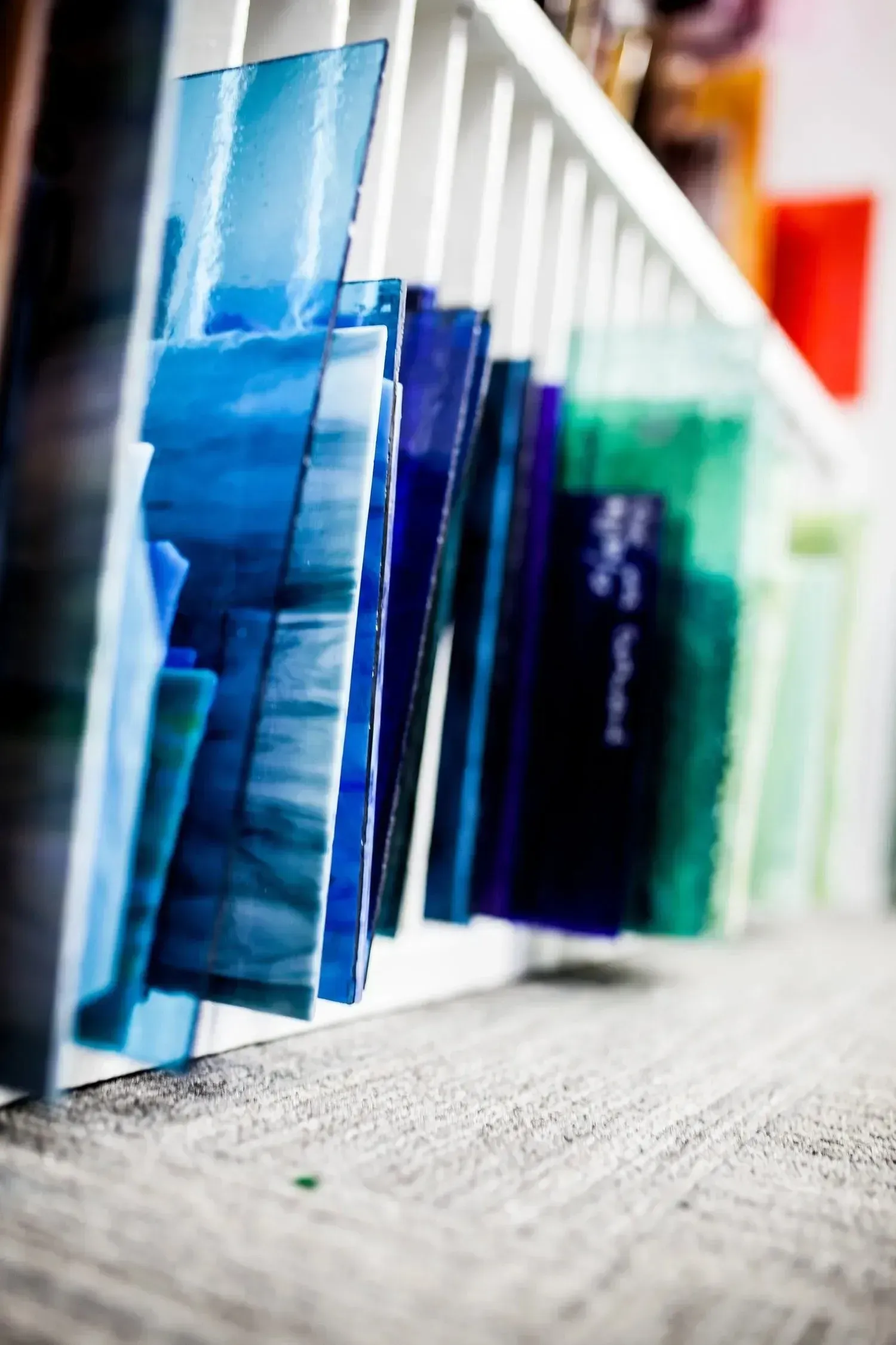 Stacks of blue and green glass sheets in a white shelf, used for art projects.