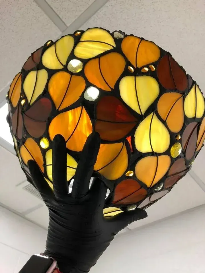 Person holding a stained glass lamp shade in the shape of leaves, various shades of yellow, brown, and orange.