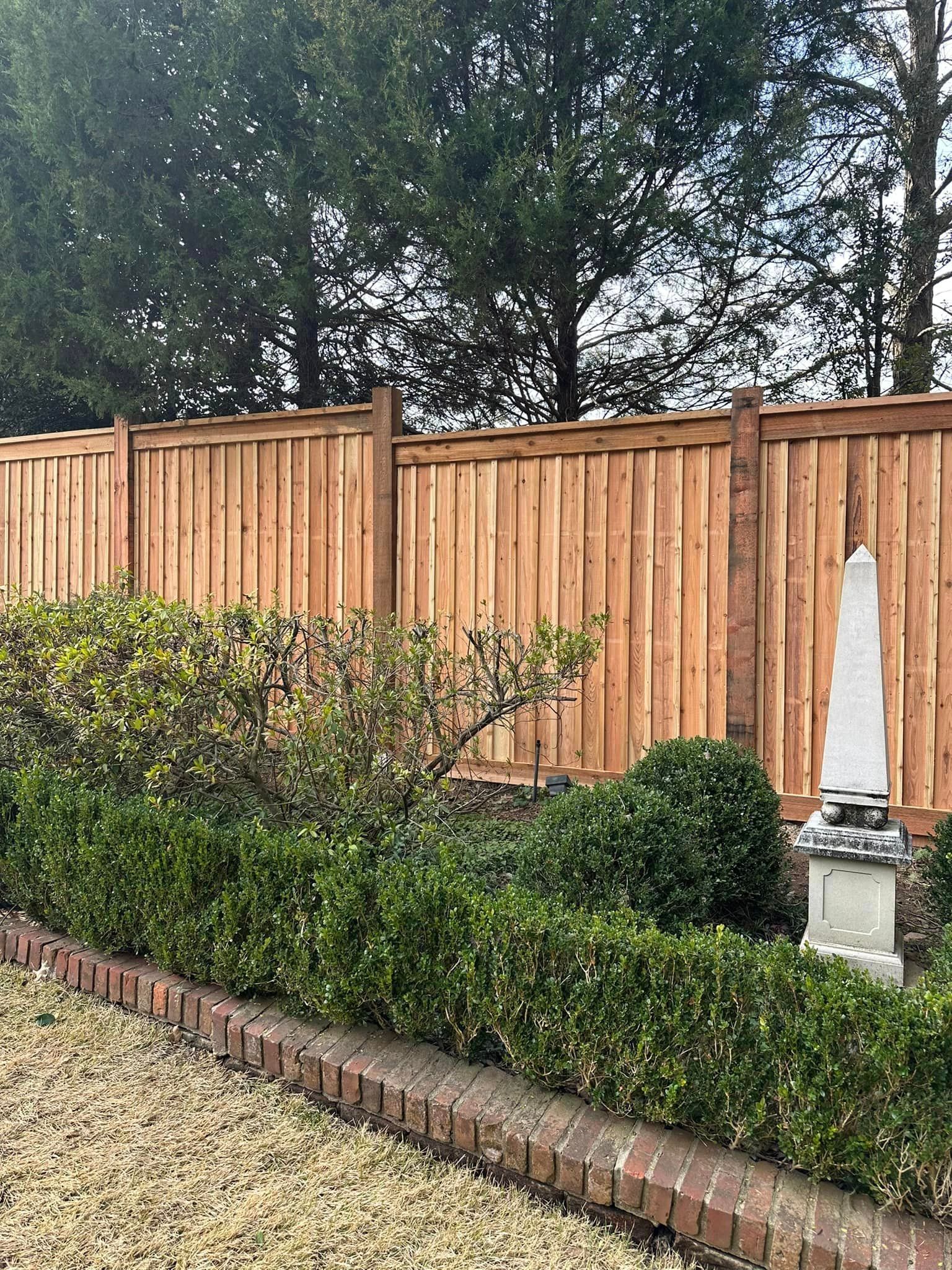 A wooden fence is surrounded by bushes and trees in a garden.