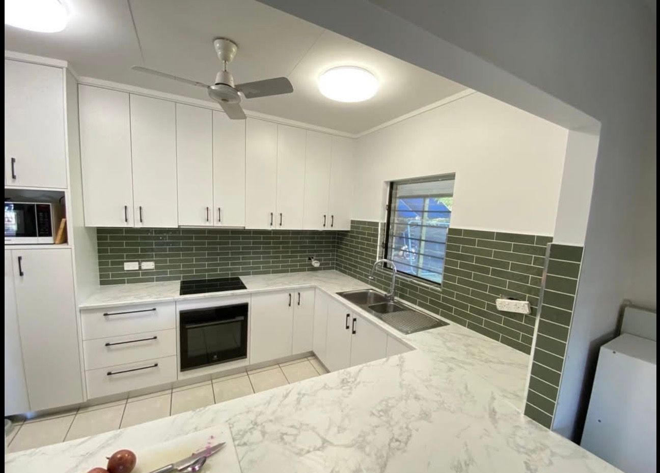 A modern kitchen featuring white cabinets, a marble-patterned countertop, and green brick-style backsplash tiles. — Frenchy’s Plaster & Paint in Bellamack, NT
