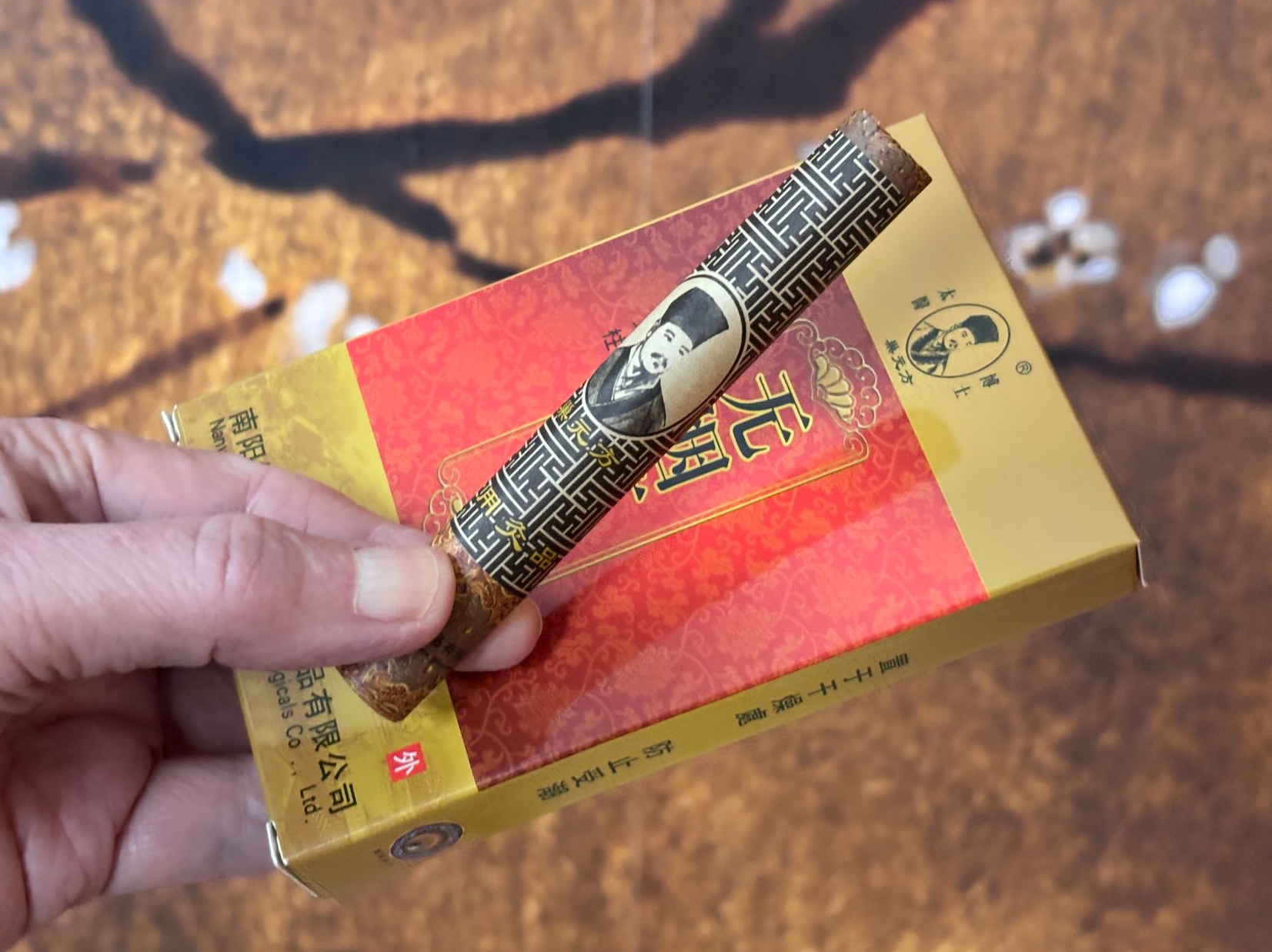 Hand die een goud-rood moxapakje vasthoudt met één moxa stick erop, buiten.