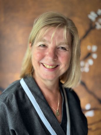 Lachende vrouw in een donkergrijze mantel tegen een warme bruine achtergrond.