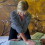 Vrouw in een gestreepte blazer demonstreert een massagetechniek op een massagetafel.