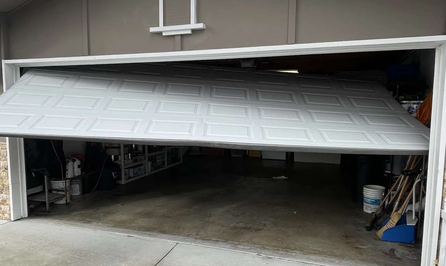 Open garage door, gray panel, revealing garage interior with tools and equipment.