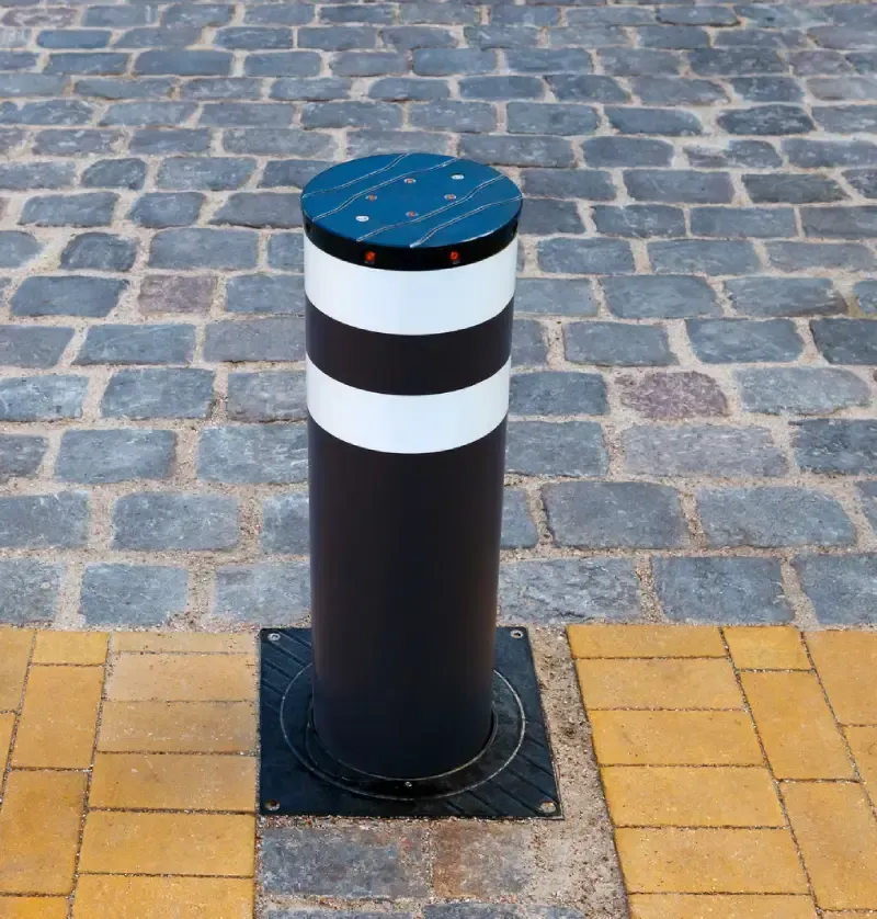 Black bollard with white bands and a blue top on a cobblestone sidewalk.