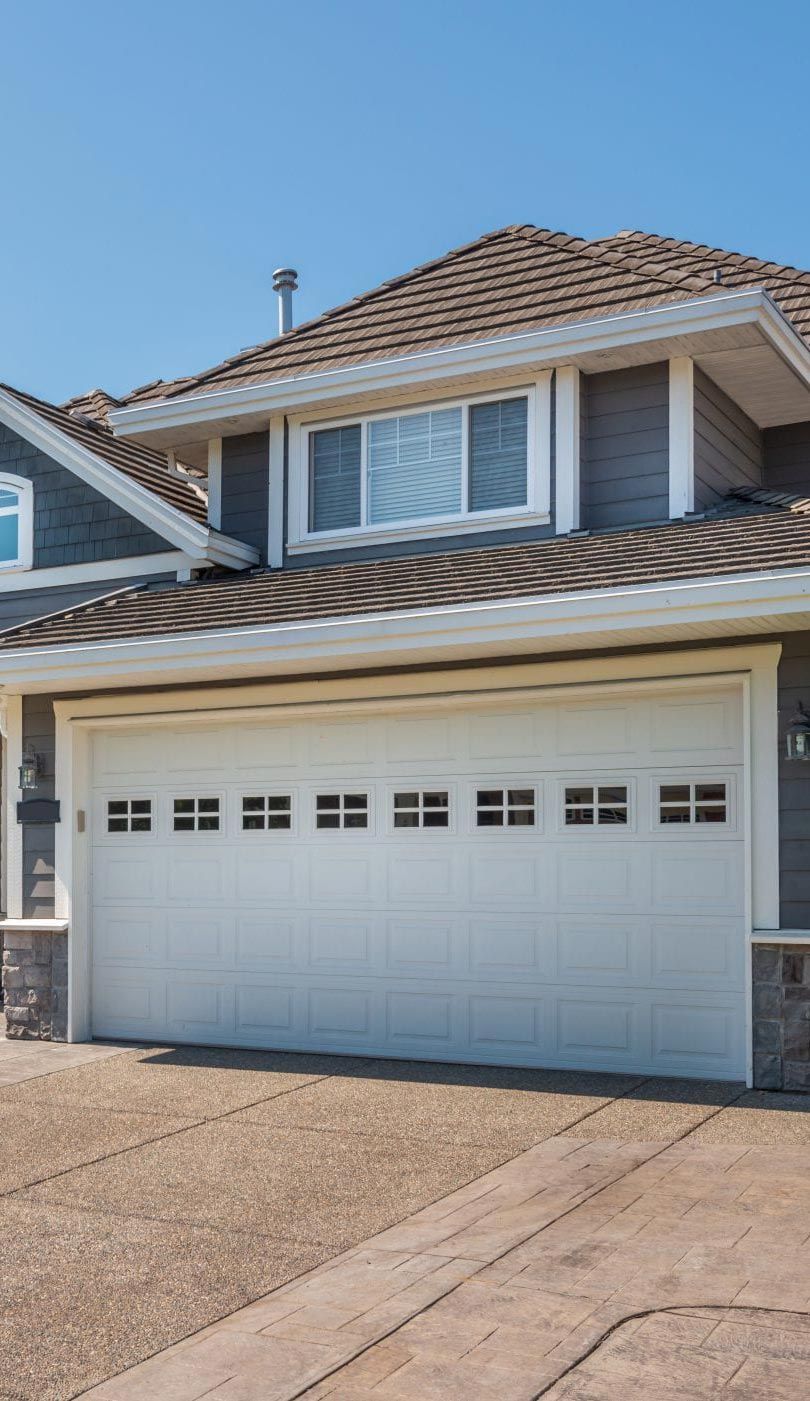 Two-story house with a tan exterior, stone accents, and two garage doors under a blue sky.
