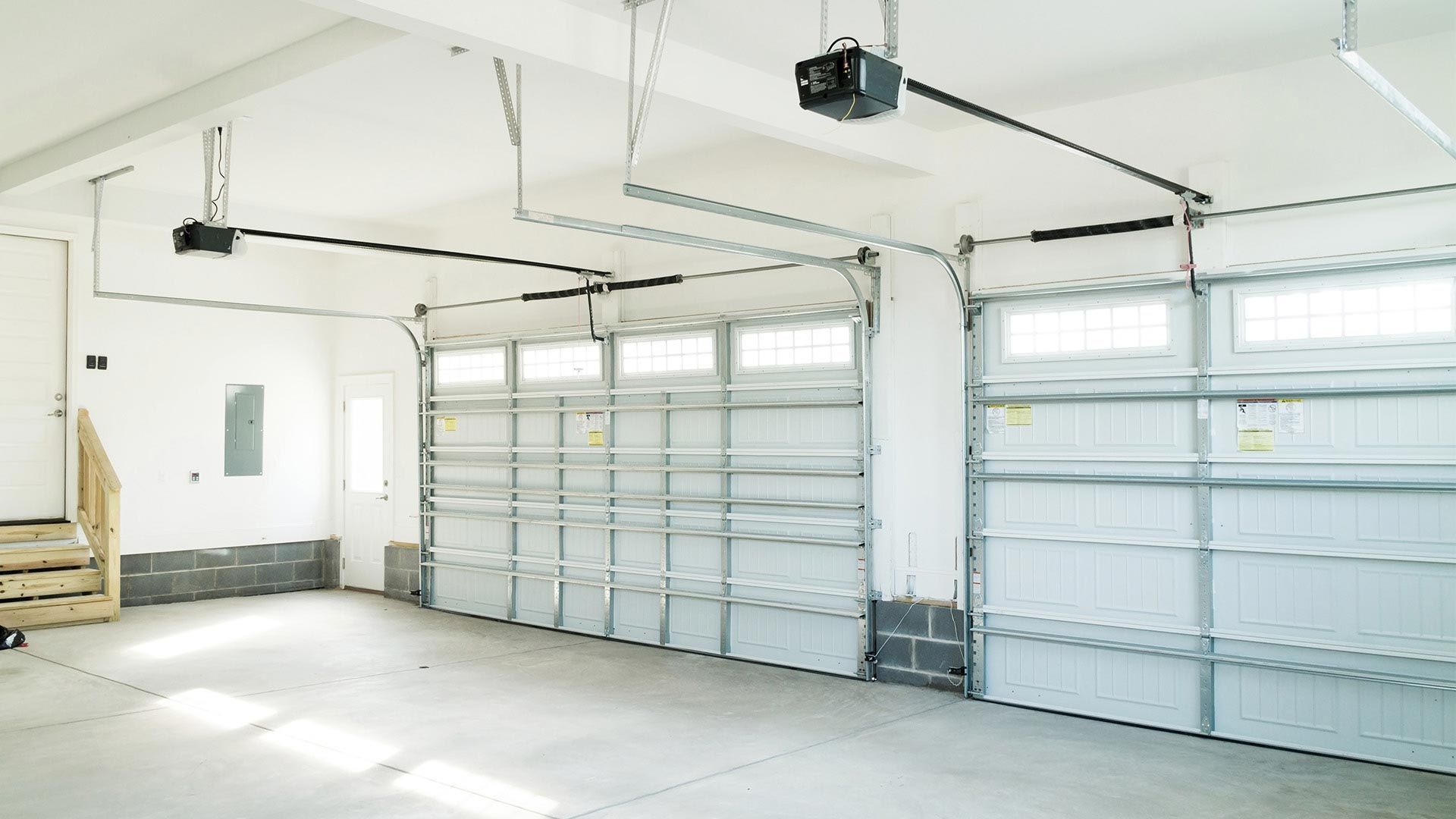 Empty garage with two overhead doors, garage door openers, and windows above doors.