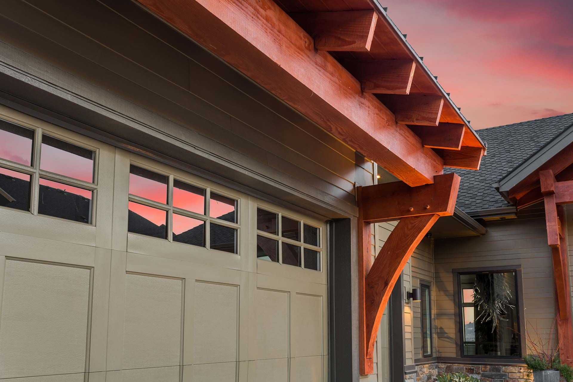 Two-story house with a tan exterior, stone accents, and two garage doors under a blue sky.