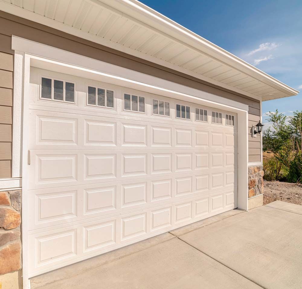 Two-story house with a tan exterior, stone accents, and two garage doors under a blue sky.