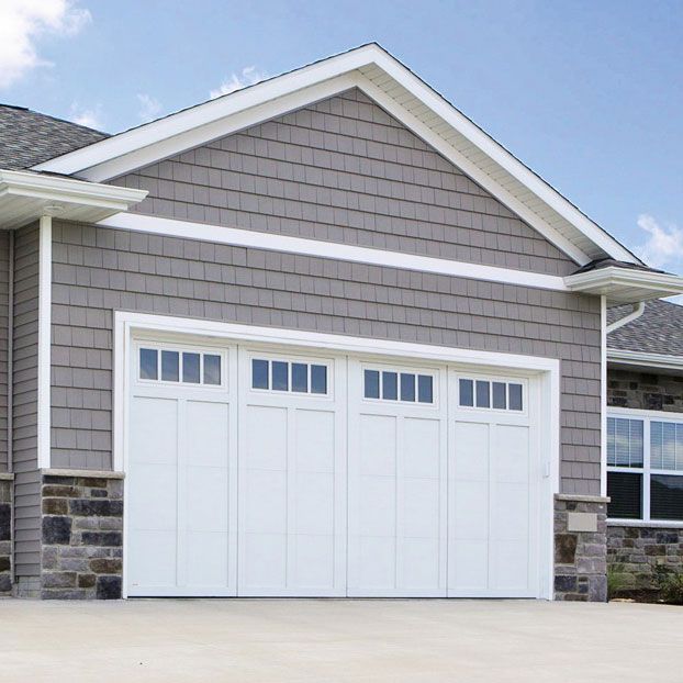 White garage doors with windows on a house with gray siding and a blue sky.