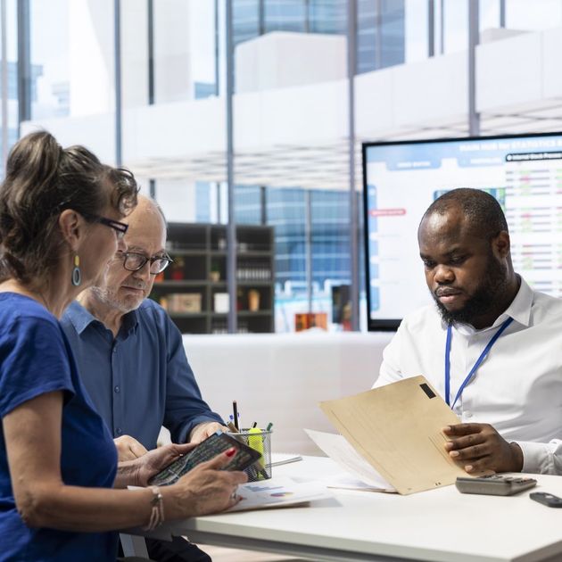 Three coworkers review documents at a table in a bright office conference room.
