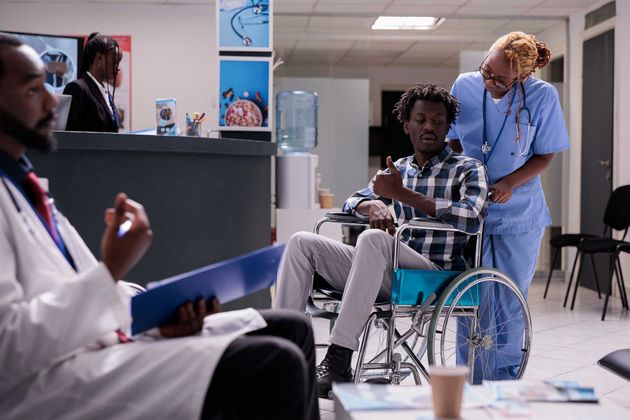 Hospital waiting room with a clinician speaking to a seated patient in a wheelchair while another staff member stands nearby