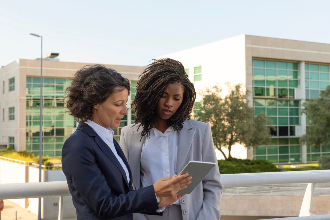 Two professionals reviewing a tablet outside a modern office building