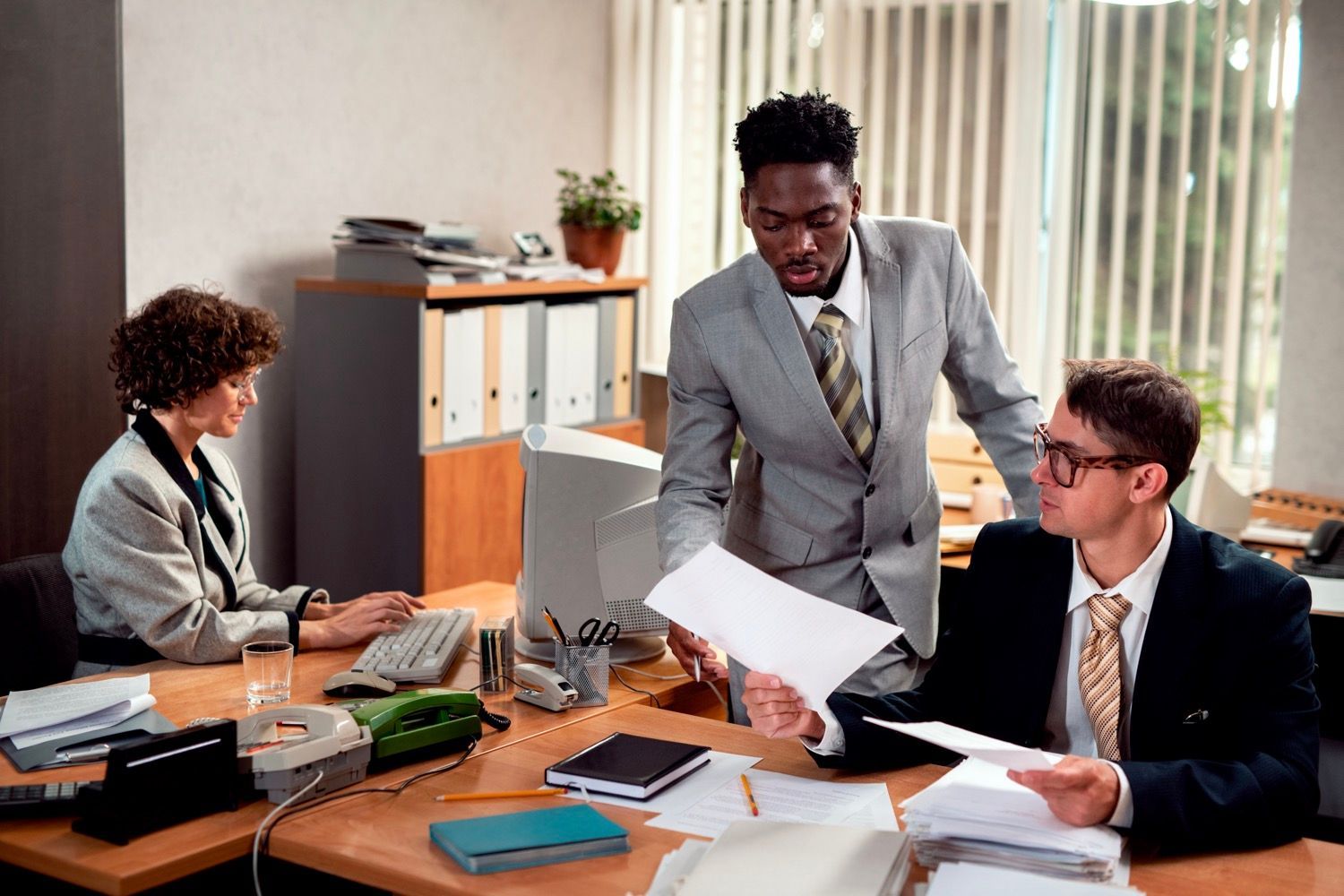 Three coworkers discuss papers around a conference table in a bright office.
