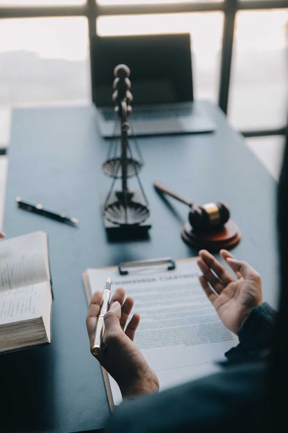 Hands reviewing a document at a desk with a gavel, scales, and laptop in the background