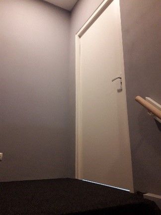 Trappenhuisoverloop met een gesloten witte deur en grijze muren, gezien vanaf de onderkant.
