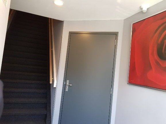 Binnenhal met zwarte trap, grijze deur en rode abstracte muurdecoratie