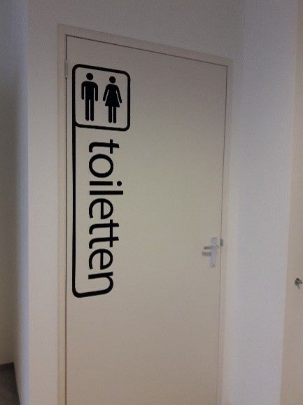 Witte badkamerdeur met bordjes voor dames- en herentoiletten en het woord 