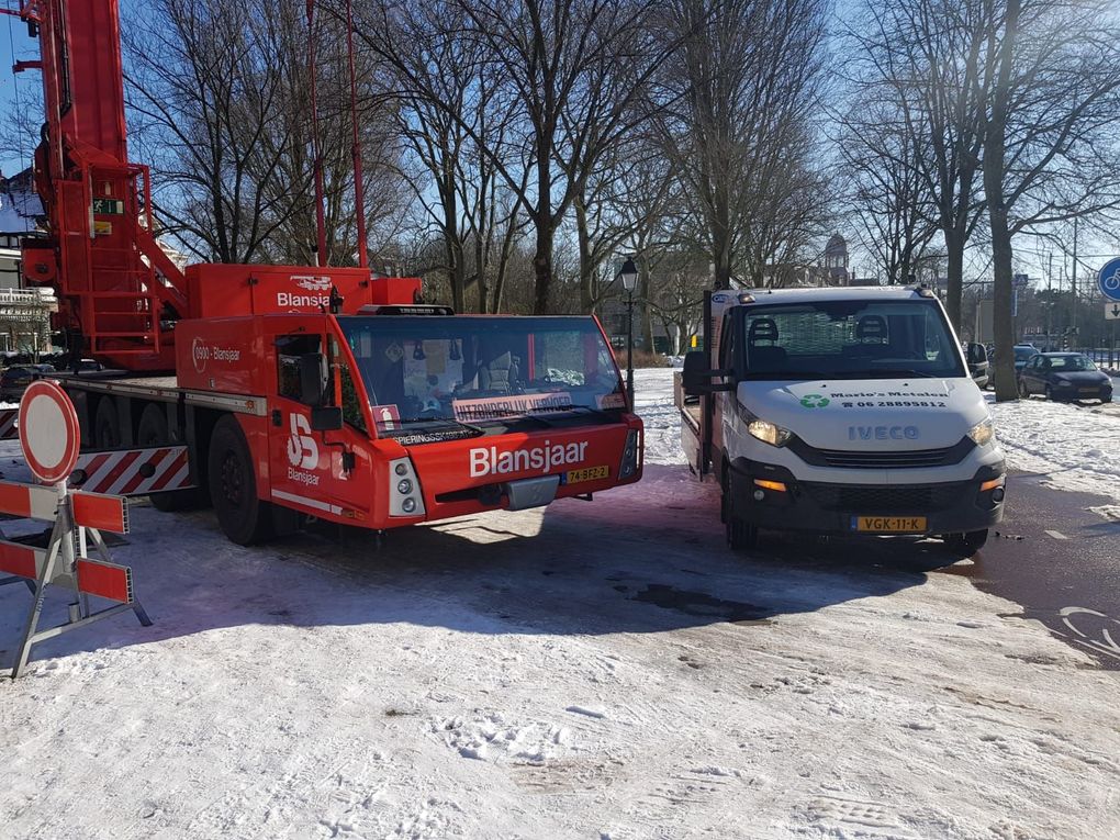 Een rode kraanwagen en een witte bestelbus staan ​​geparkeerd op een besneeuwd terrein naast verkeersborden.