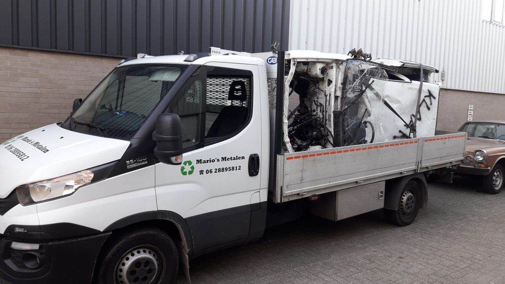 Witte vrachtwagen met open laadbak, waarvan de laadruimte achterin is uitgebrand, staat geparkeerd naast een magazijn.