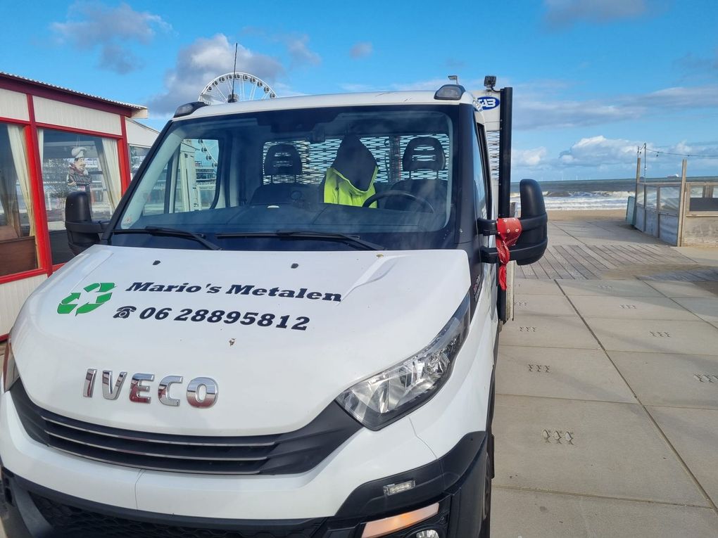 Witte Iveco-bestelbus geparkeerd aan de waterkant, met een chauffeur erin en bedrijfslogo op de motorkap.