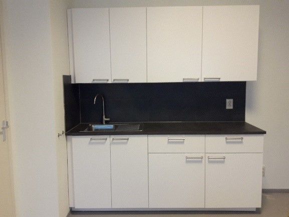 Witte kastjes en een zwart aanrechtblad in een kleine kitchenette met spoelbak en bovenkastjes.