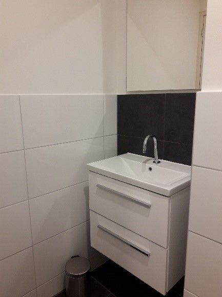Kleine badkamerwastafel met wit badmeubel, zwarte achterwand en een prullenbak eronder.