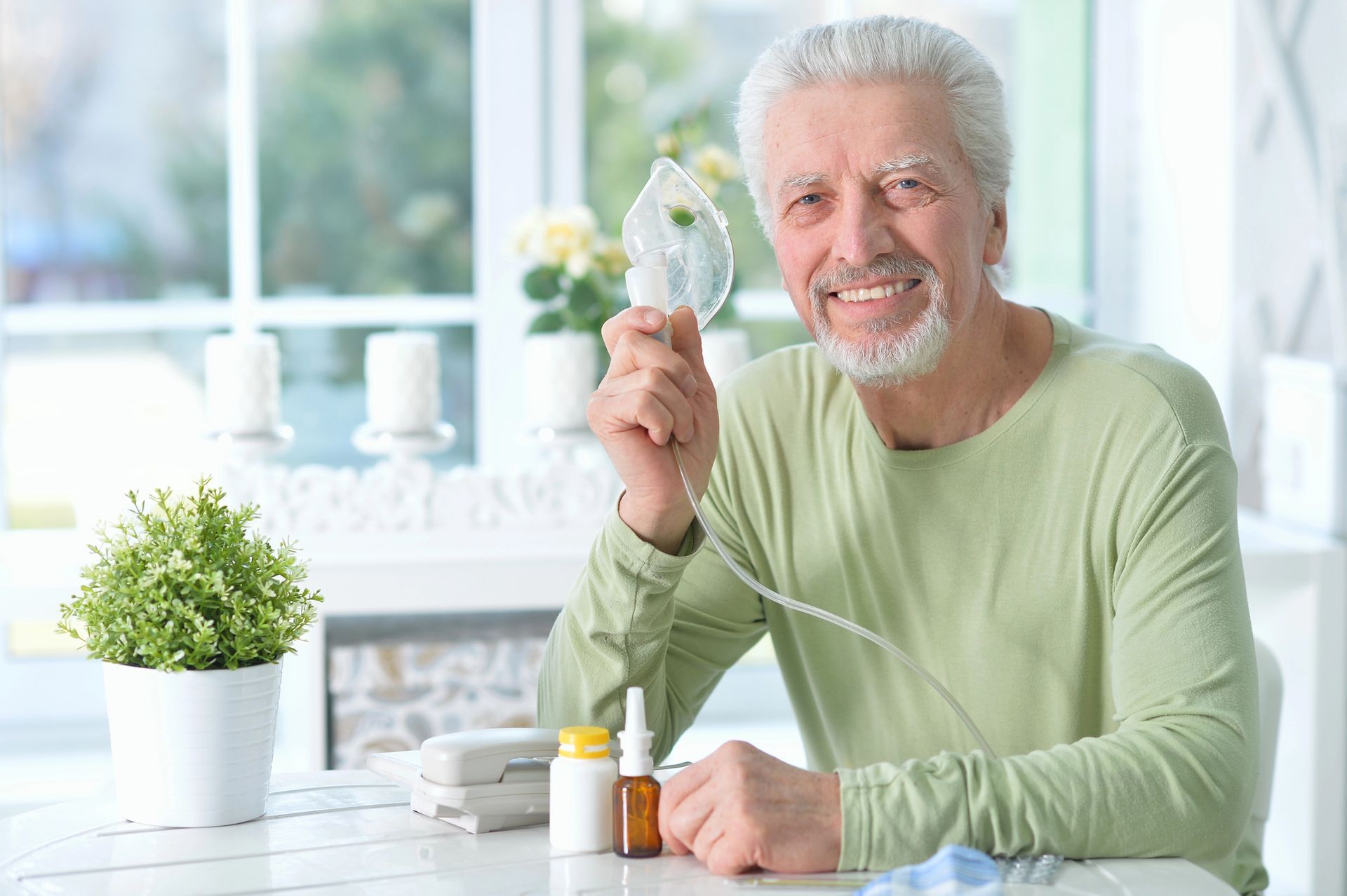 Hombre sonriente sentado a una mesa sosteniendo un inhalador nasal transparente en un entorno doméstico luminoso.