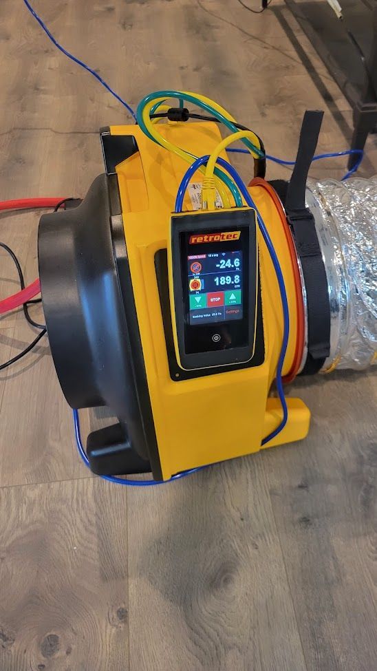 Yellow portable HVAC unit with digital display and coiled hoses on a floor, next to silver ducting.