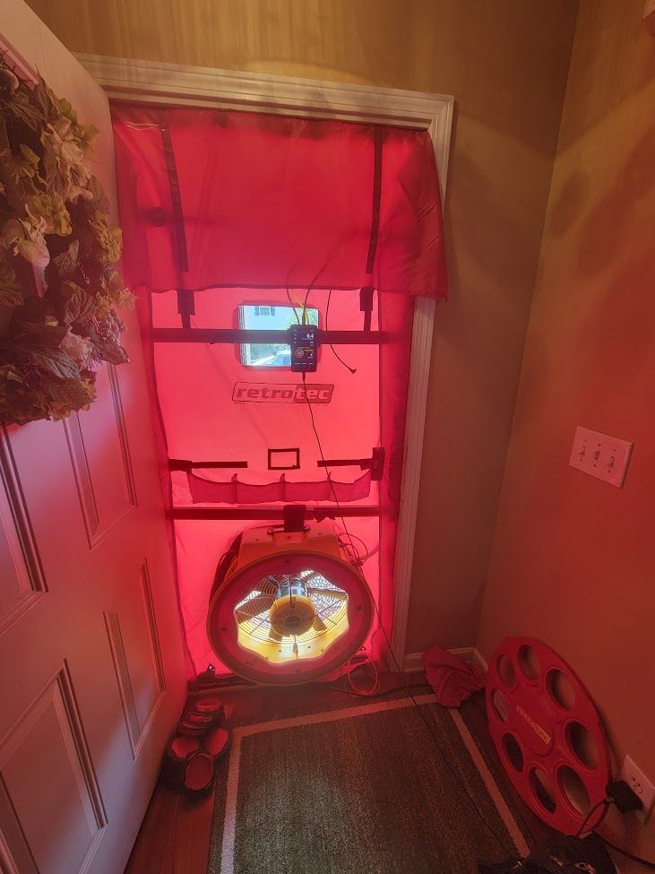 Hallway with a blower door test setup, red-tinted plastic cover, and testing fan in the doorway