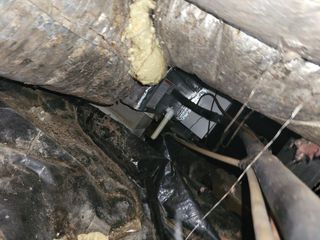 Collapsed insulation and debris in a dark crawlspace with exposed pipes and wiring.