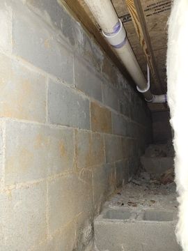 Narrow crawl space with cinder block walls, overhead pipe, and debris on the floor